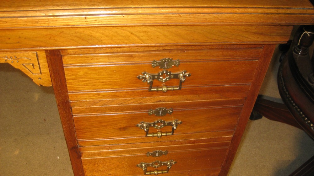 A late Victorian golden walnut pedestal desk featuring a dark leather-inlaid writing top, twin pedestals with stacked drawers, carved kneehole spandrels, and brass drop handles. View III