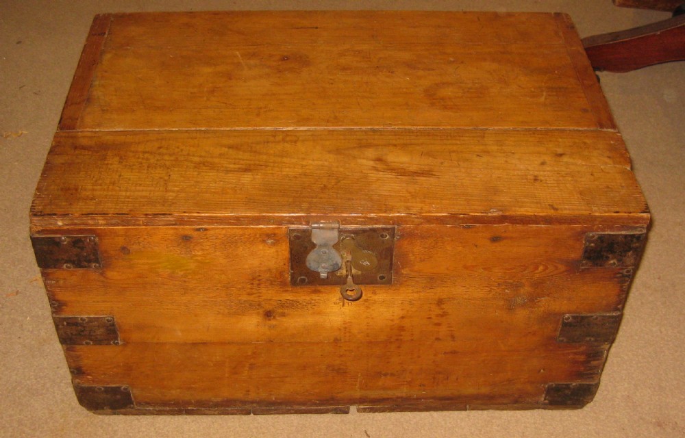 A rectangular solid pine storage trunk featuring iron corner brackets and a central metal lock mechanism with key.