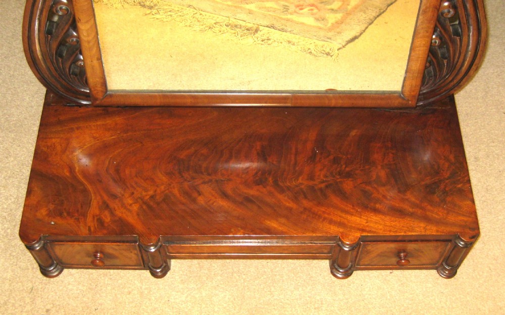 A Victorian flame mahogany swing dressing mirror featuring carved scroll upright supports and a rectangular tilting glass resting on a base with drawers. View IX