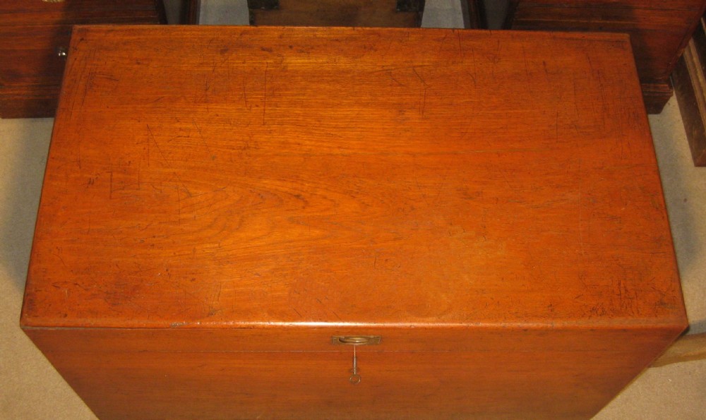 A rectangular Victorian solid teak wooden trunk featuring a hinged top lid, a central flush brass catch, and a keyhole on the front panel. View II