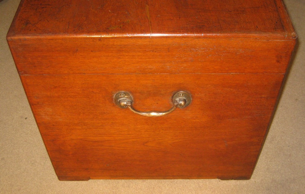 A rectangular Victorian solid teak wooden trunk featuring a hinged top lid, a central flush brass catch, and a keyhole on the front panel. View VII