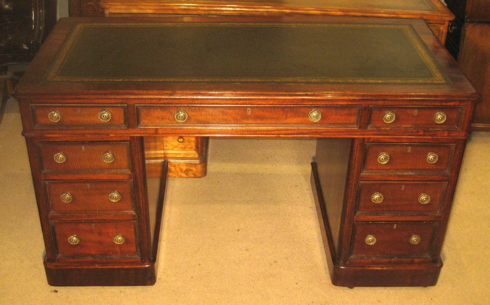 A Victorian mahogany pedestal desk featuring a dark green leather writing surface with gold tooling, multiple drawers with round brass handles, and solid plinth bases.