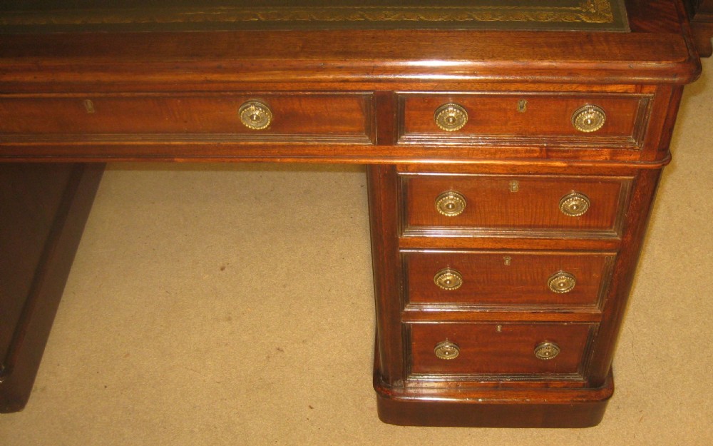 A Victorian mahogany pedestal desk featuring a dark green leather writing surface with gold tooling, multiple drawers with round brass handles, and solid plinth bases. View II