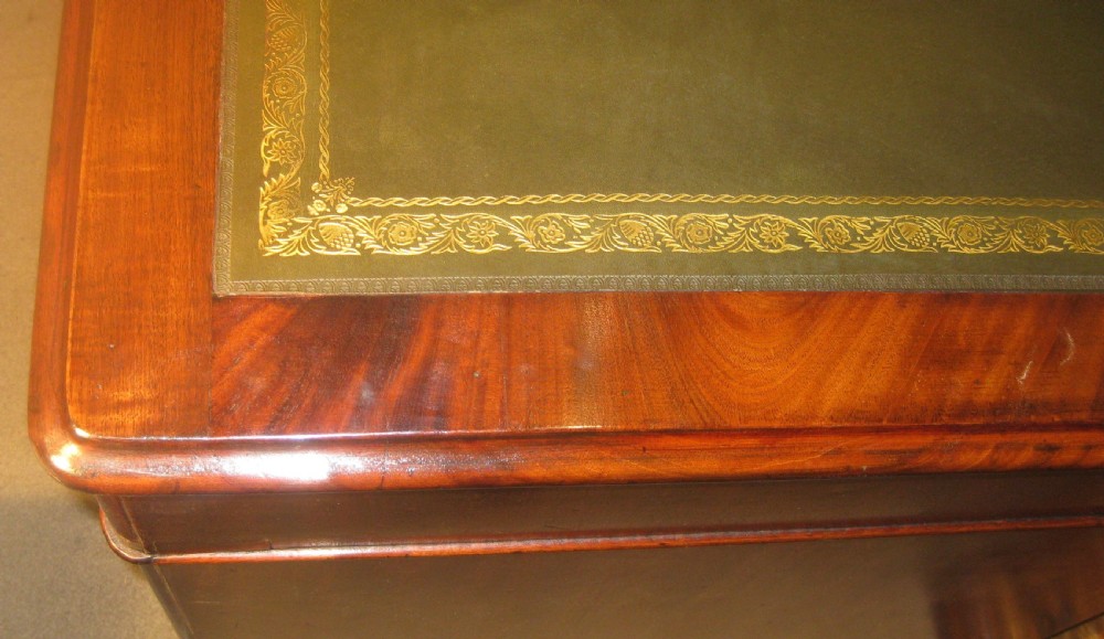 A Victorian mahogany pedestal desk featuring a dark green leather writing surface with gold tooling, multiple drawers with round brass handles, and solid plinth bases. View VI