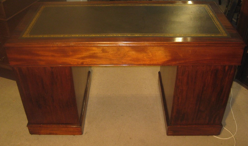 A Victorian mahogany pedestal desk featuring a dark green leather writing surface with gold tooling, multiple drawers with round brass handles, and solid plinth bases. View VII
