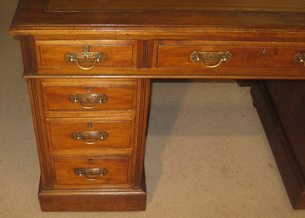 Victorian mahogany pedestal desk featuring a gold-tooled brown leather writing surface, brass handles, and two drawer pedestals on plinth bases. View II