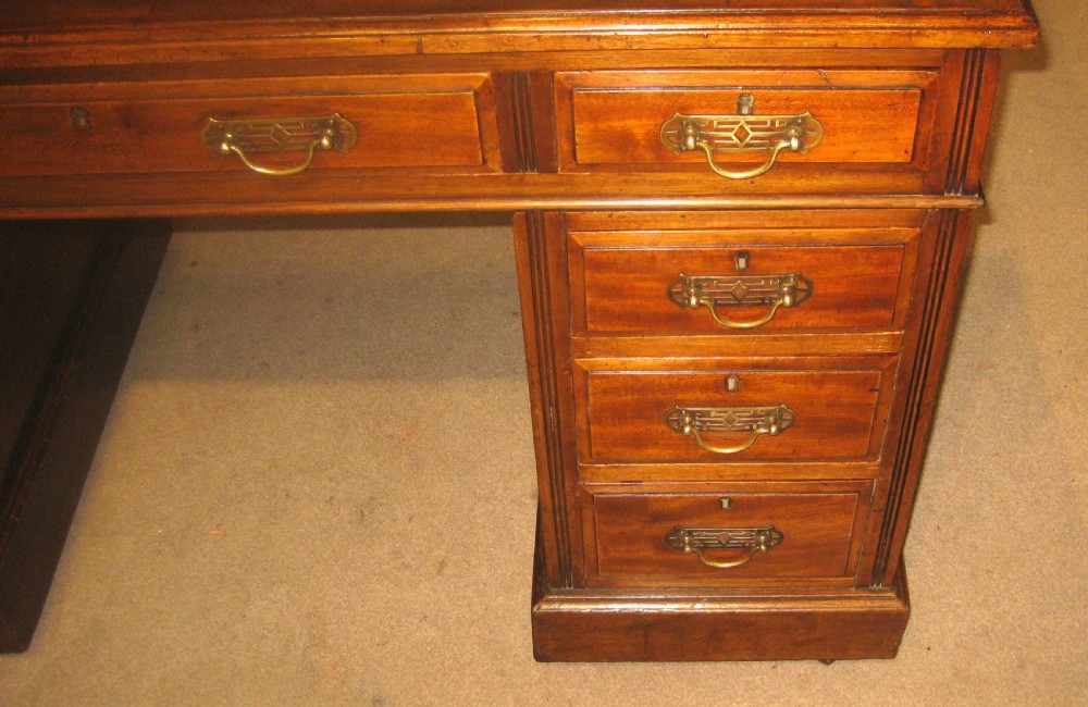 Victorian mahogany pedestal desk featuring a gold-tooled brown leather writing surface, brass handles, and two drawer pedestals on plinth bases. View VII