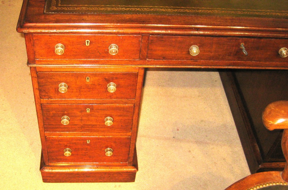 A Victorian mahogany pedestal desk featuring a green leather writing surface insert and nine storage drawers with brass knobs. View V
