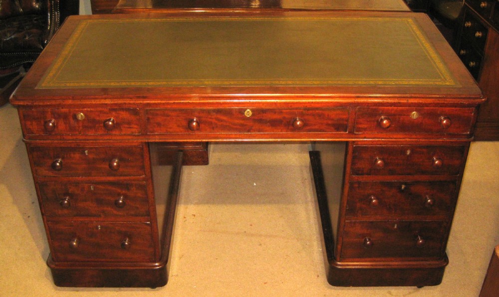 A Victorian mahogany pedestal desk featuring nine drawers with turned handles, rounded corners, and a green leather insert.