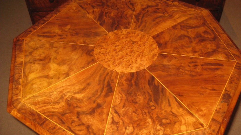 An octagonal burr walnut occasional table with segmentally veneered top resting on a carved central column and tripod legs with castors. View IV