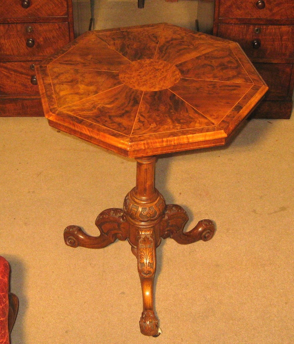 An octagonal burr walnut occasional table with segmentally veneered top resting on a carved central column and tripod legs with castors.