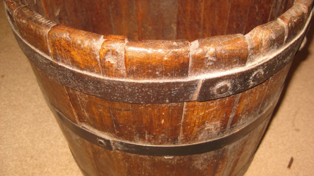 An antique coopered oak well bucket featuring vertical timber staves, two wrought iron metal bands, and a curved iron swing handle. View IV