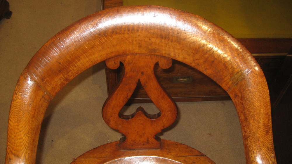 Victorian golden oak desk chair with a curved backrest, carved central splat, green leather padded seat, and turned front legs on brass castors. View V