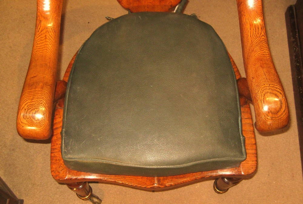 Victorian golden oak desk chair with a curved backrest, carved central splat, green leather padded seat, and turned front legs on brass castors. View X