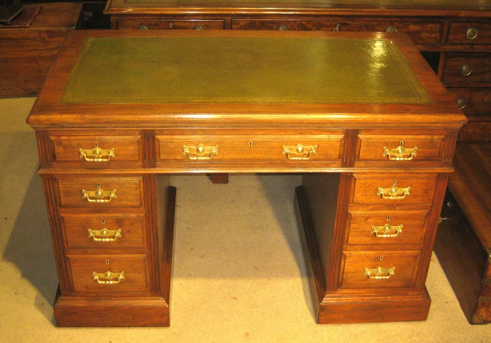 A Victorian solid walnut pedestal desk featuring a green gilt-tooled leather writing surface, nine drawers with brass drop handles, and a plinth base.
