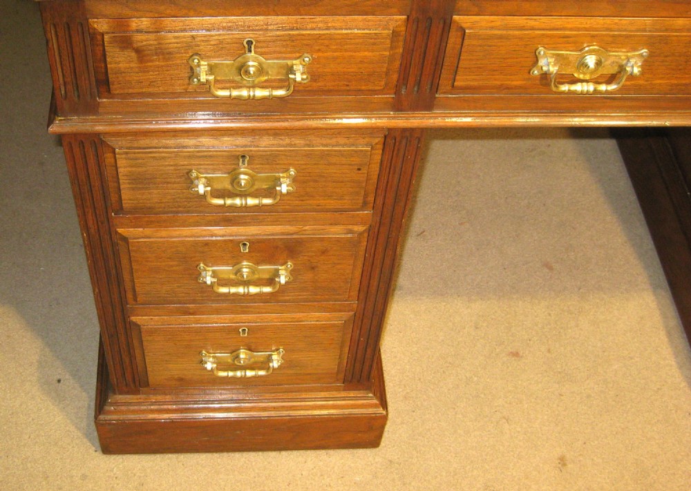 A Victorian solid walnut pedestal desk featuring a green gilt-tooled leather writing surface, nine drawers with brass drop handles, and a plinth base. View II