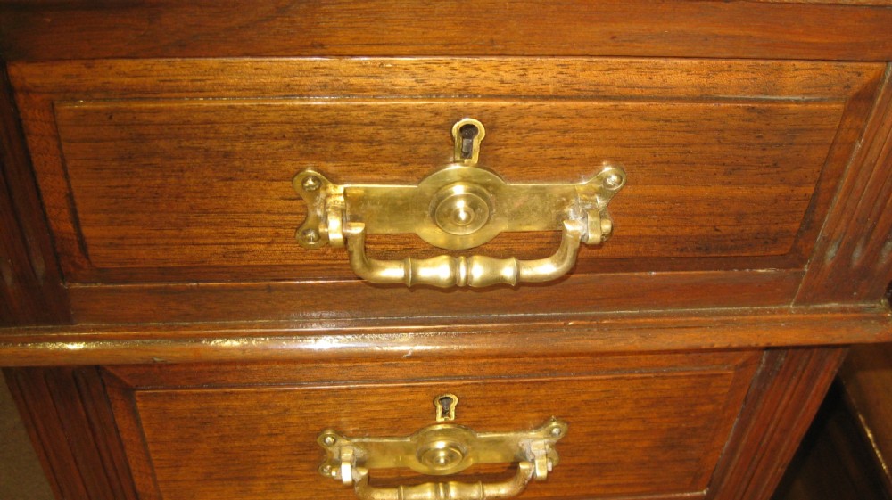 A Victorian solid walnut pedestal desk featuring a green gilt-tooled leather writing surface, nine drawers with brass drop handles, and a plinth base. View III