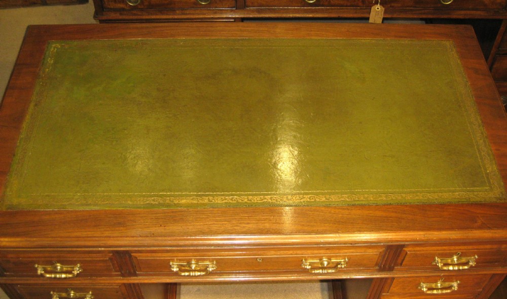 A Victorian solid walnut pedestal desk featuring a green gilt-tooled leather writing surface, nine drawers with brass drop handles, and a plinth base. View IV