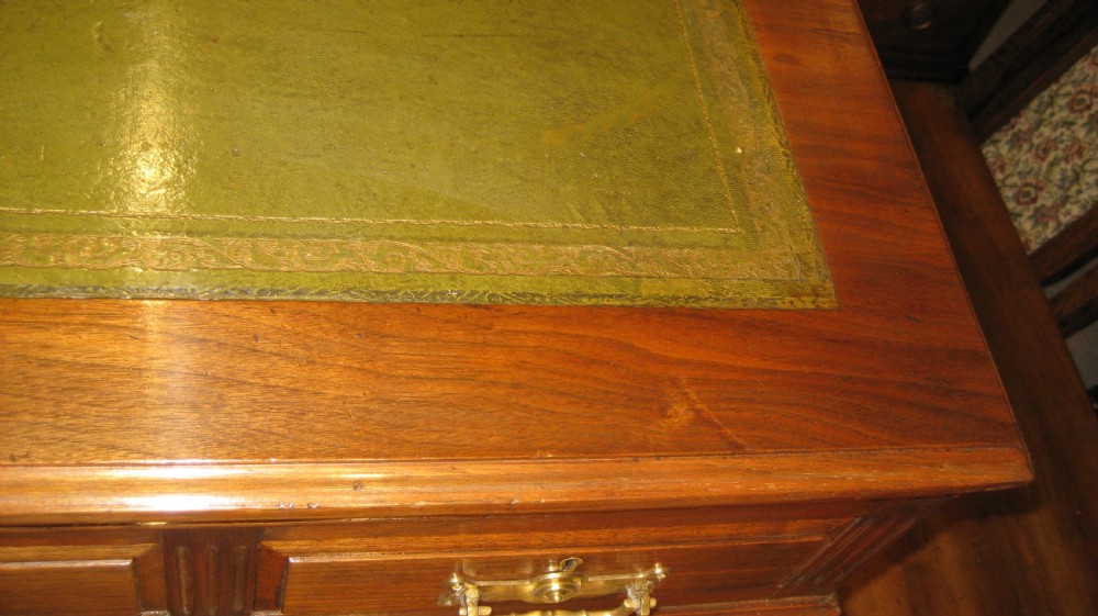 A Victorian solid walnut pedestal desk featuring a green gilt-tooled leather writing surface, nine drawers with brass drop handles, and a plinth base. View V