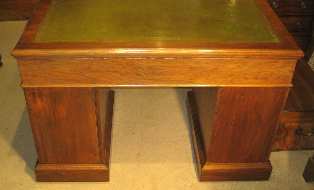 A Victorian solid walnut pedestal desk featuring a green gilt-tooled leather writing surface, nine drawers with brass drop handles, and a plinth base. View IX