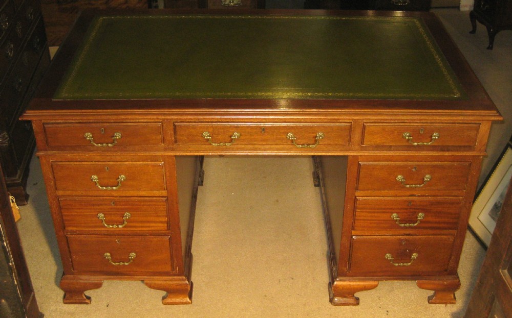 A late Victorian solid mahogany pedestal desk featuring a green leather gilt-tooled writing skiver top, nine drawers with brass handles, and a central kneehole.