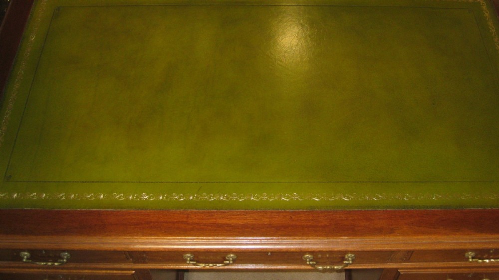 A late Victorian solid mahogany pedestal desk featuring a green leather gilt-tooled writing skiver top, nine drawers with brass handles, and a central kneehole. View II