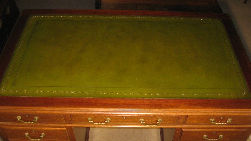 A late Victorian solid mahogany pedestal desk featuring a green leather gilt-tooled writing skiver top, nine drawers with brass handles, and a central kneehole. View III