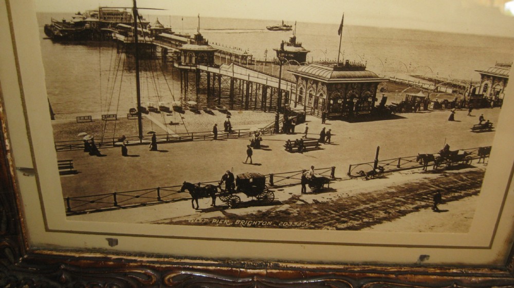 A pair of matching dark carved wooden frames containing sepia-toned historical photographs of the pier and seafront at Brighton. View III