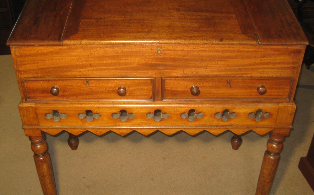 An early Victorian golden mahogany clerks desk featuring a sloped lid, upper gallery panel, two small drawers, gothic quatrefoil frieze, and turned legs. View II