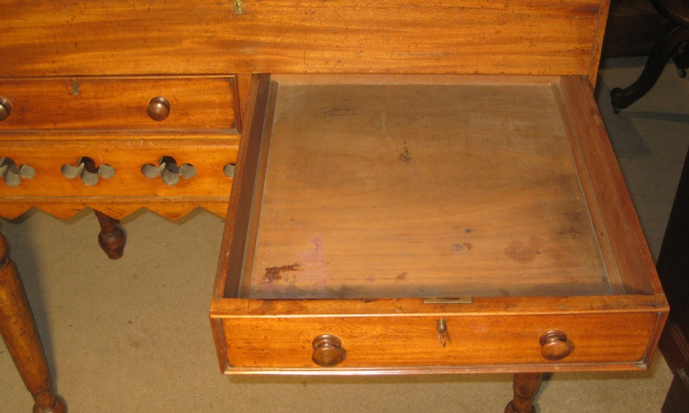 An early Victorian golden mahogany clerks desk featuring a sloped lid, upper gallery panel, two small drawers, gothic quatrefoil frieze, and turned legs. View VI
