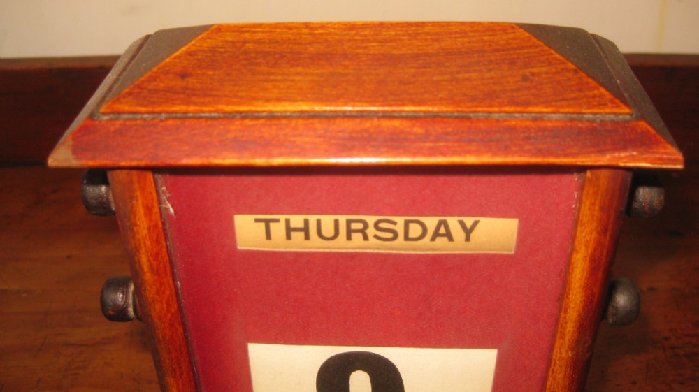 An Edwardian mahogany desktop perpetual calendar with side turning knobs and a red fabric facade displaying day, date, and month. View IV