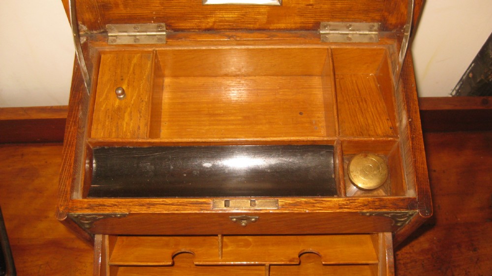 An Edwardian oak stationery cabinet featuring decorative brass corner mounts, a brass shield-shaped cartouche on the lid, and a central brass handle. View III