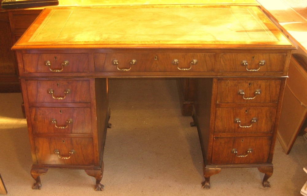 A late Victorian walnut pedestal desk featuring a leather-lined writing surface, multiple drawers with brass swan-neck handles, and carved cabriole feet.