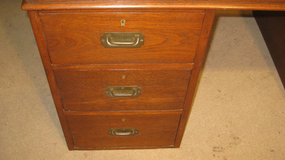 A late Victorian solid teak pedestal campaign desk featuring a gilt-tooled leather writing surface and flush brass drawer handles. View II