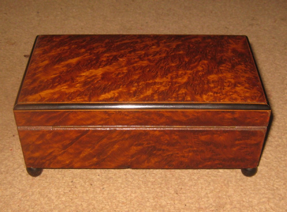A rectangular Victorian box veneered in warm brown amboyna wood with dark ebony borders and small feet.