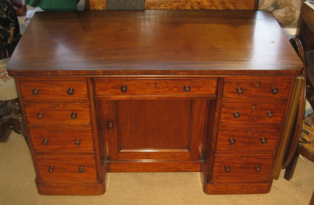 Victorian flame mahogany kneehole desk featuring multiple side drawers with turned wooden knobs and a central recessed cupboard on a plinth base.