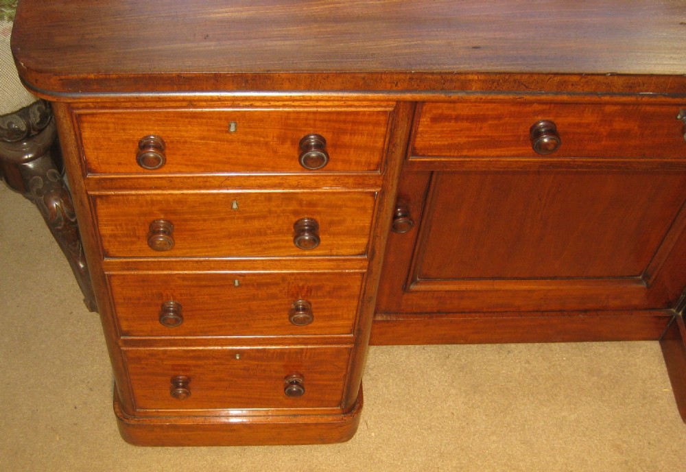 Victorian flame mahogany kneehole desk featuring multiple side drawers with turned wooden knobs and a central recessed cupboard on a plinth base. View II