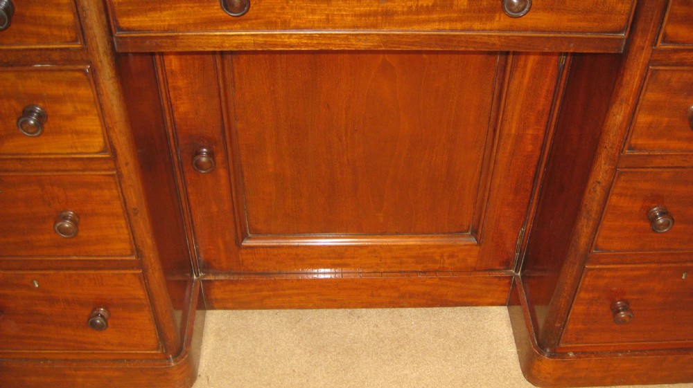 Victorian flame mahogany kneehole desk featuring multiple side drawers with turned wooden knobs and a central recessed cupboard on a plinth base. View III