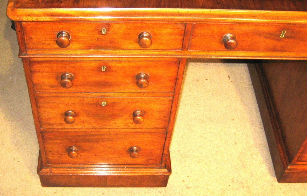 A Victorian mahogany pedestal desk featuring a green leather inset writing surface, nine drawers with turned wooden knobs, and a plinth base. View II