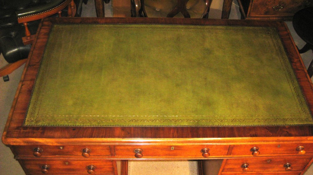 A Victorian mahogany pedestal desk featuring a green leather inset writing surface, nine drawers with turned wooden knobs, and a plinth base. View IV
