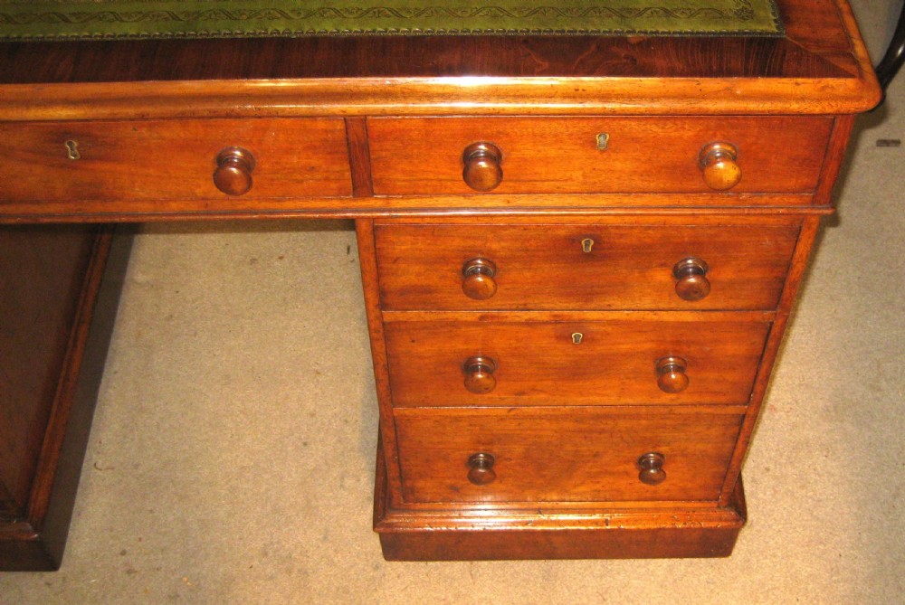 A Victorian mahogany pedestal desk featuring a green leather inset writing surface, nine drawers with turned wooden knobs, and a plinth base. View V