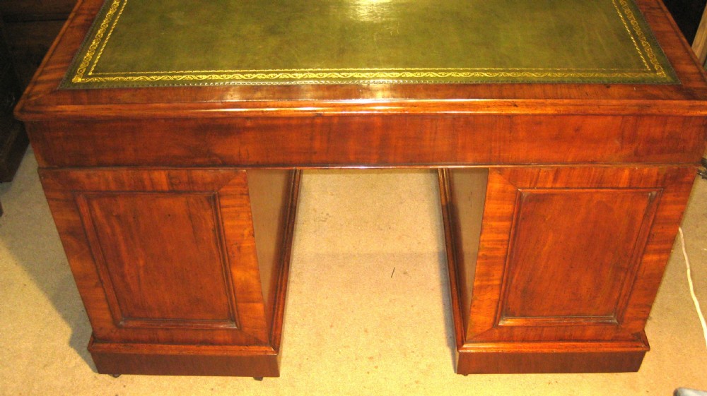 A Victorian mahogany pedestal desk featuring a green leather inset writing surface, nine drawers with turned wooden knobs, and a plinth base. View VII