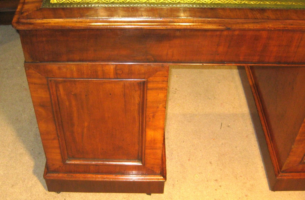 A Victorian mahogany pedestal desk featuring a green leather inset writing surface, nine drawers with turned wooden knobs, and a plinth base. View IX