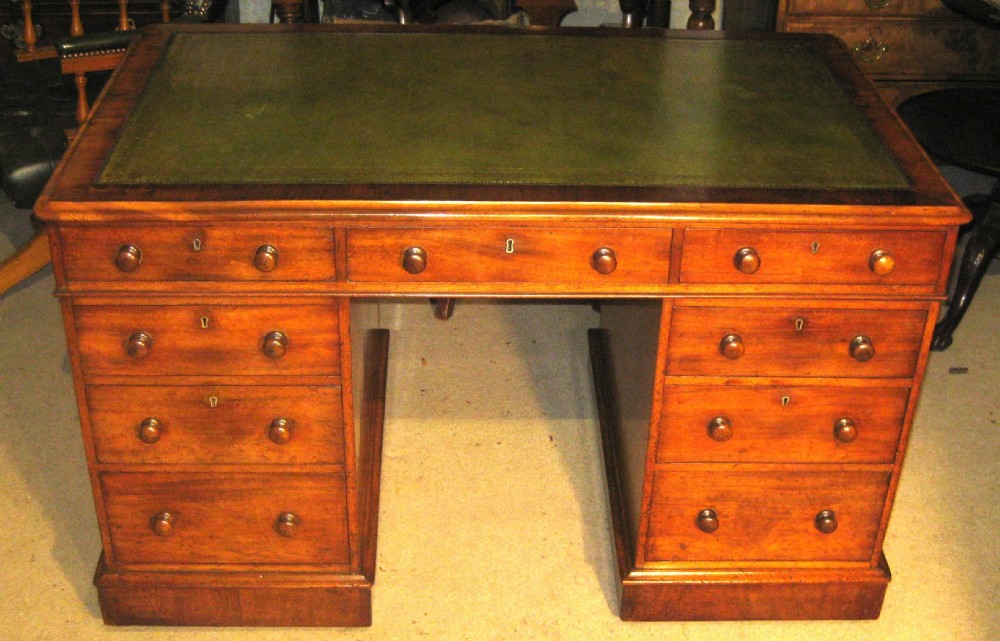 A Victorian mahogany pedestal desk featuring a green leather inset writing surface, nine drawers with turned wooden knobs, and a plinth base.