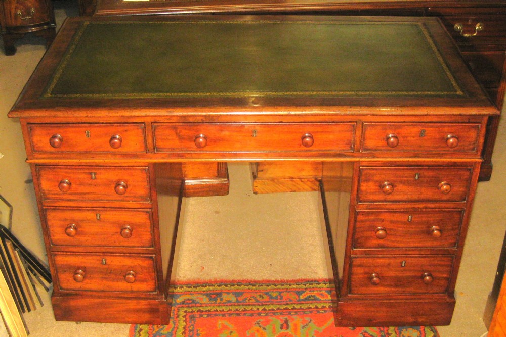 A late Victorian mahogany pedestal desk featuring a dark green gilt-tooled leather writing surface, multiple drawers with turned wooden knob handles, and twin pedestals on plinth bases.