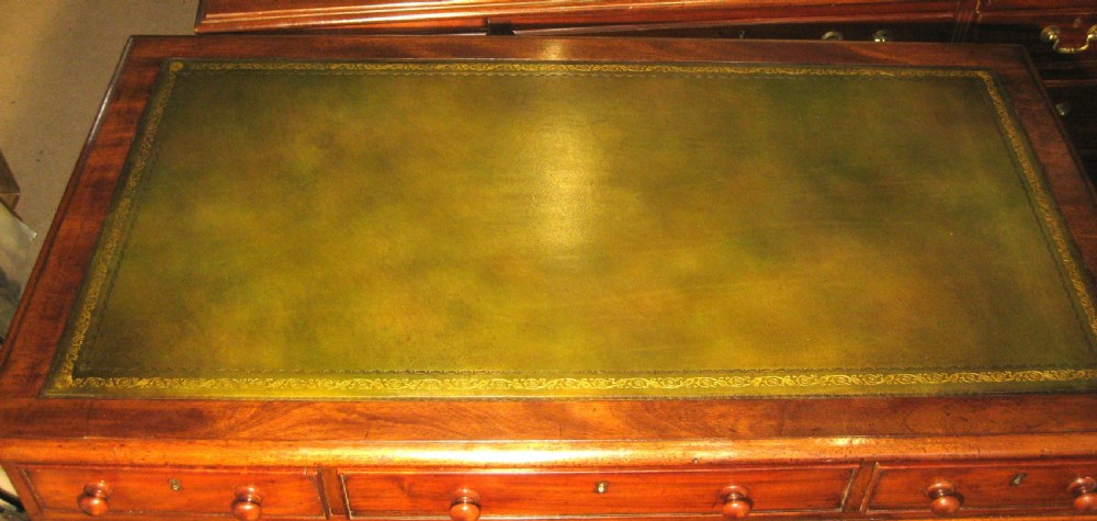 A late Victorian mahogany pedestal desk featuring a dark green gilt-tooled leather writing surface, multiple drawers with turned wooden knob handles, and twin pedestals on plinth bases. View II