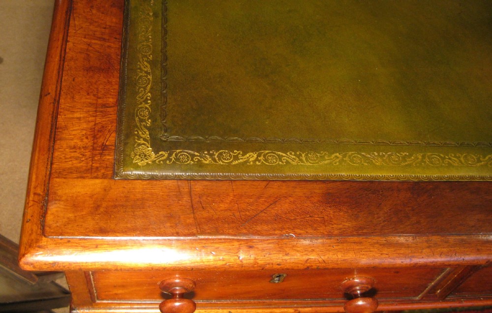 A late Victorian mahogany pedestal desk featuring a dark green gilt-tooled leather writing surface, multiple drawers with turned wooden knob handles, and twin pedestals on plinth bases. View V