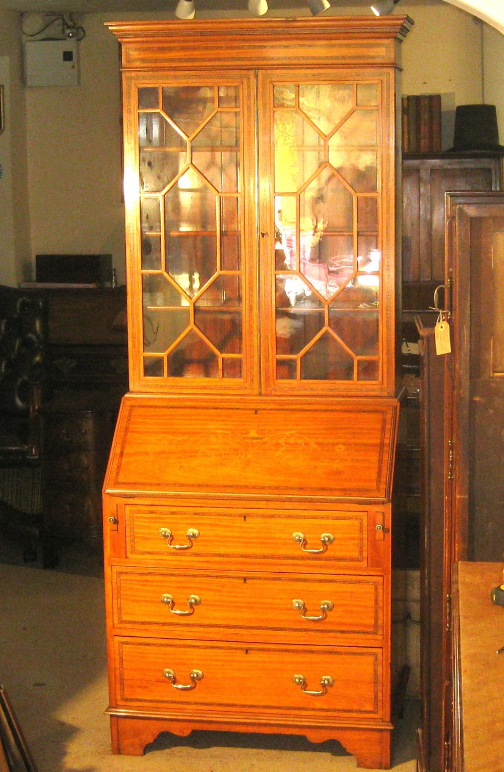 An Edwardian satinwood bureau bookcase featuring a two-door astragal glazed upper display section above a fall-front desk and three long drawers with brass handles.