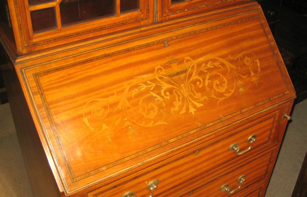 An Edwardian satinwood bureau bookcase featuring a two-door astragal glazed upper display section above a fall-front desk and three long drawers with brass handles. View V