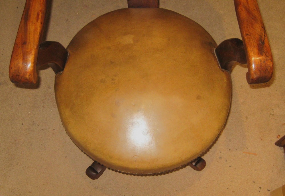 A Victorian walnut revolving desk chair featuring a curved horseshoe backrest, pierced carved splat, circular tan leather upholstered seat with brass studding, and four splayed legs on castors. View II